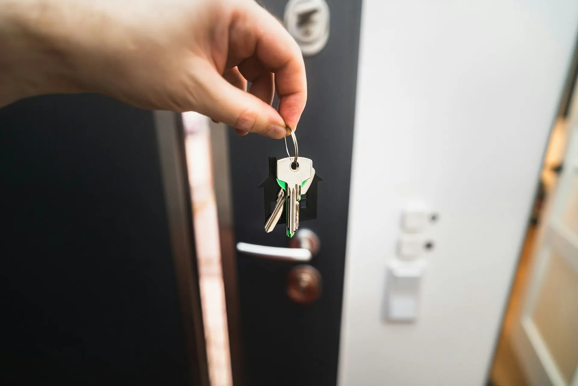 A hand holding new house keys in front of an open door